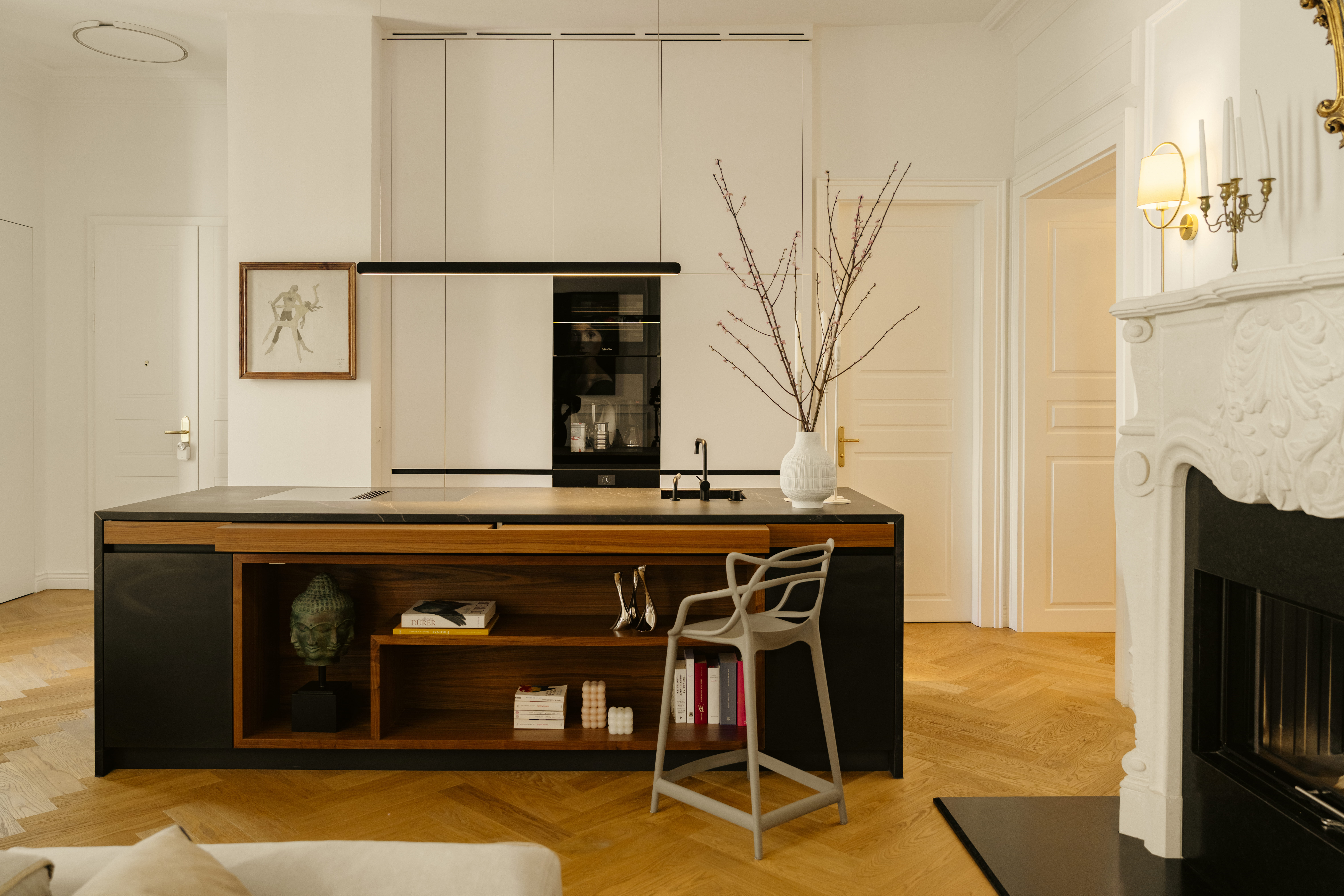 Kitchen — dark island with walnut detail, herringbone floor, marble fireplace beyond
