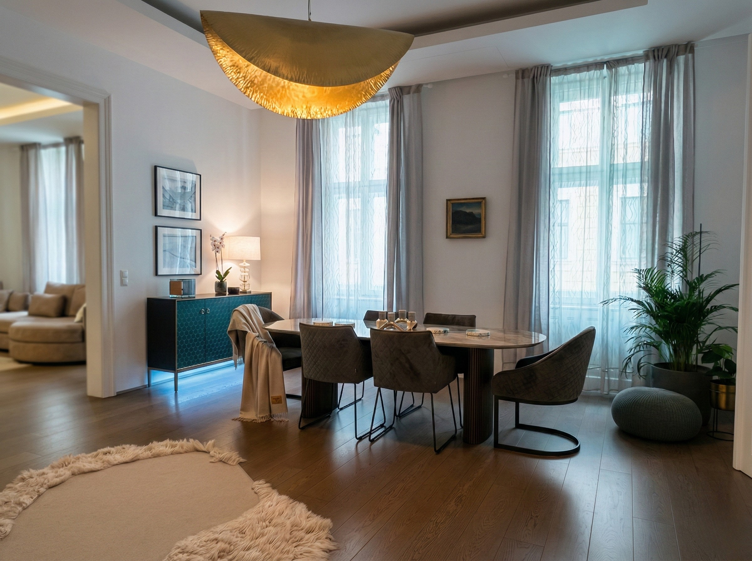 Contemporary apartment — gold crescent pendant, dining table, tall curtained windows